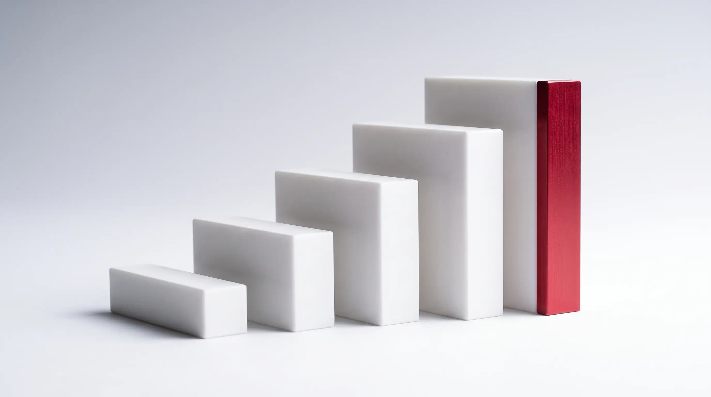 Five matte white machined blocks of ascending height arranged as a staircase, the leading edge of the tallest one red.