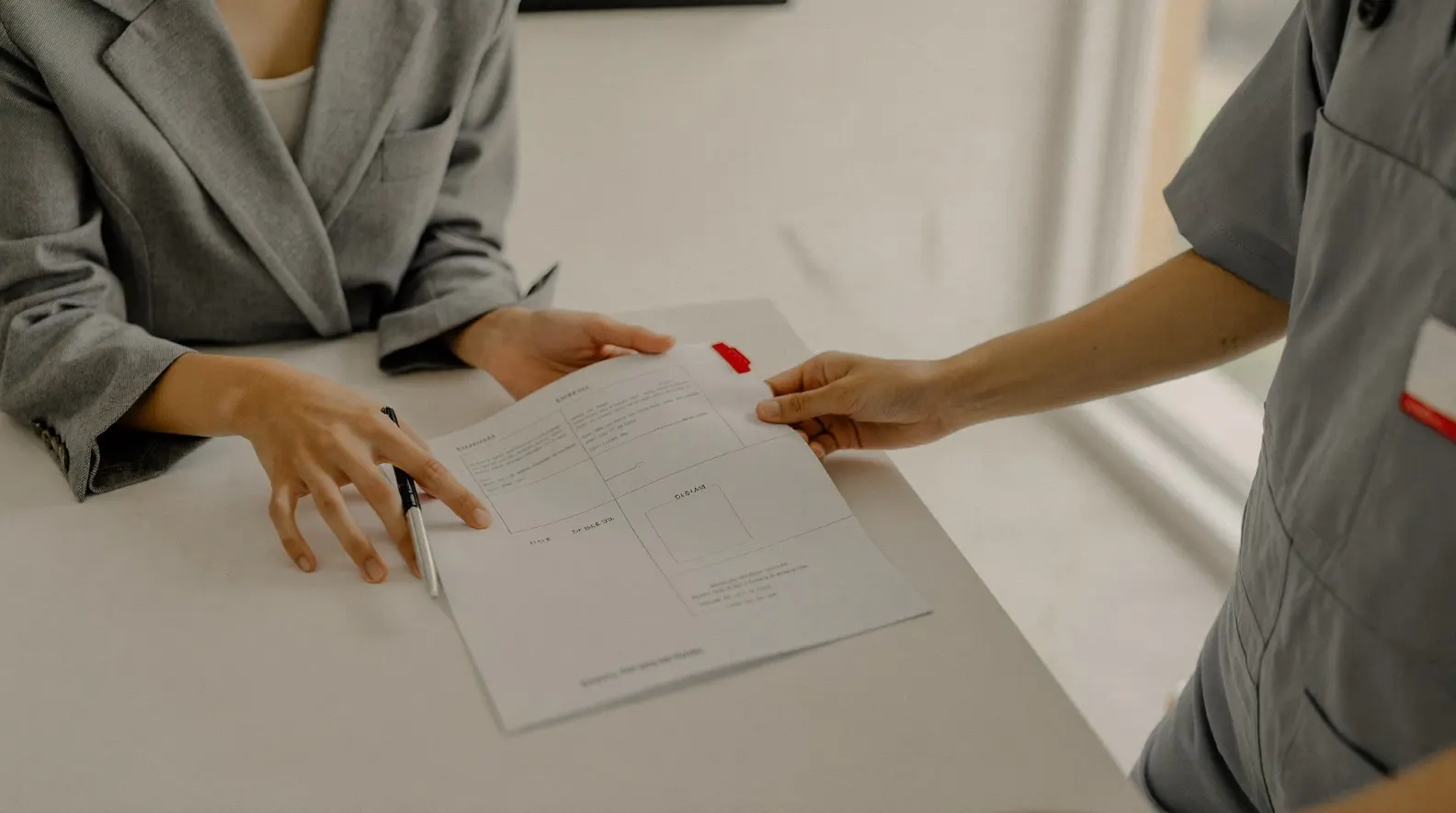 Two people at a table, one in a blazer and one in work coveralls, reviewing a printed proposal document together with a red tab bookmark on one page. An illustration of the proposal handover described in stage 03.