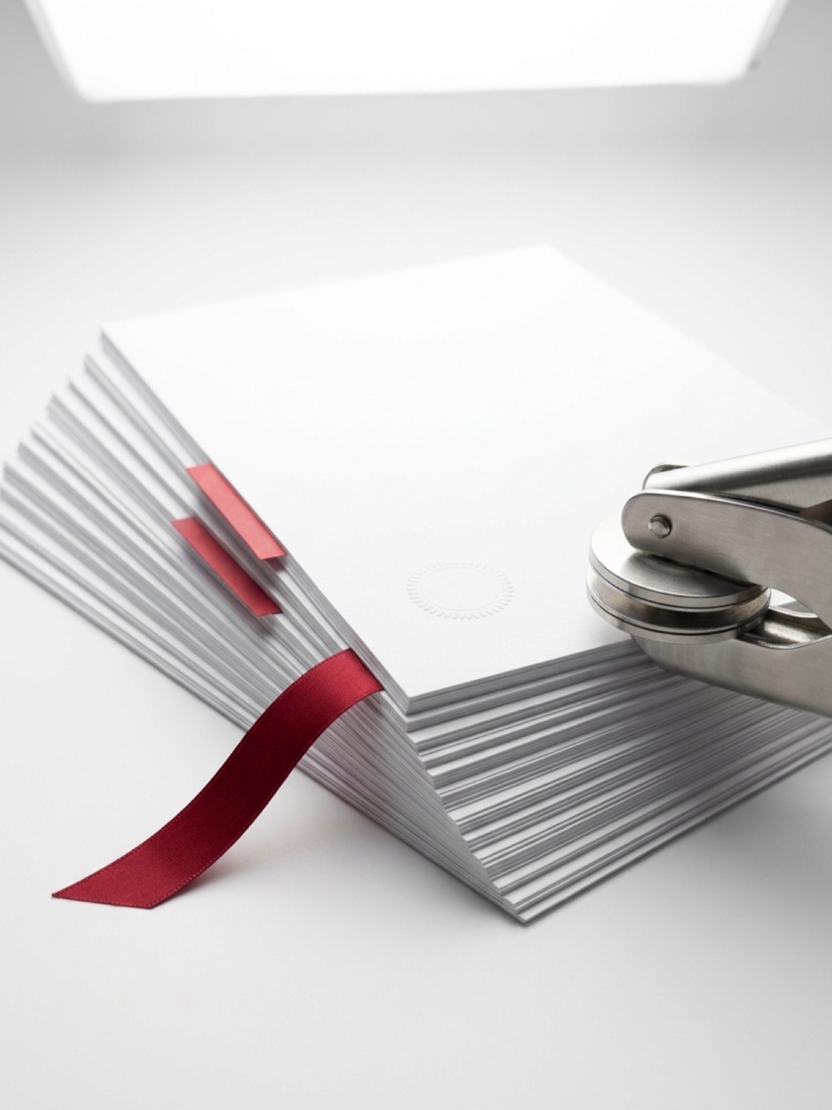 A stack of certification records with an embossing seal press, red index tabs, and a bound ribbon.