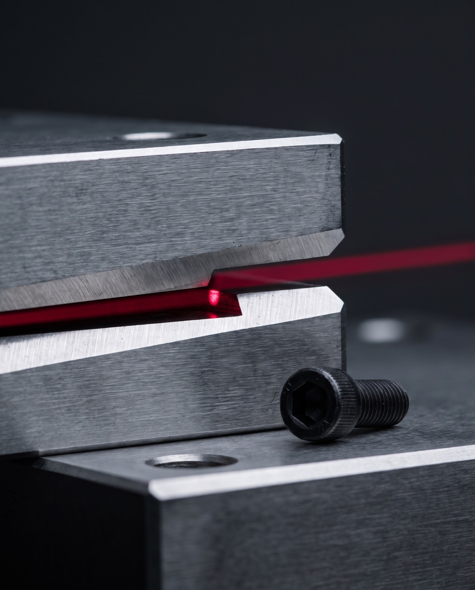 A macro view of two steel plates that have failed to seat, the red light line broken across the open joint and a bolt left loose beside it.