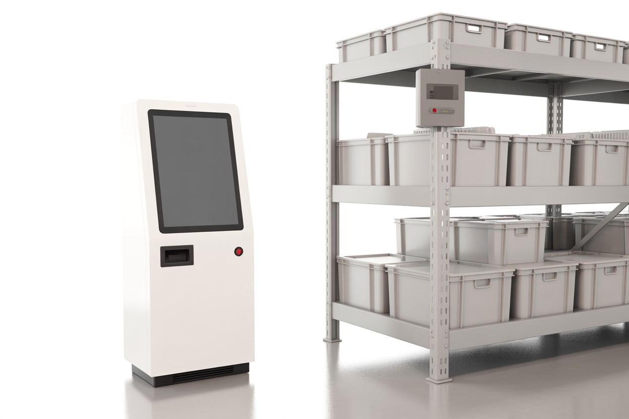 A white self-service kiosk terminal with a single red status light, beside light grey warehouse shelving holding matching storage totes, shown as a generic illustration of the class of system described.